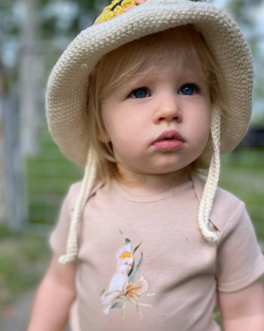 Child wearing a beige hat with ear flaps and a matching shirt outdoors.
