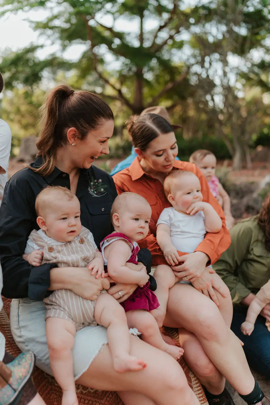 Breastfeeding half button shirt. Mums sitting together holding their babies smiling and outdoors.