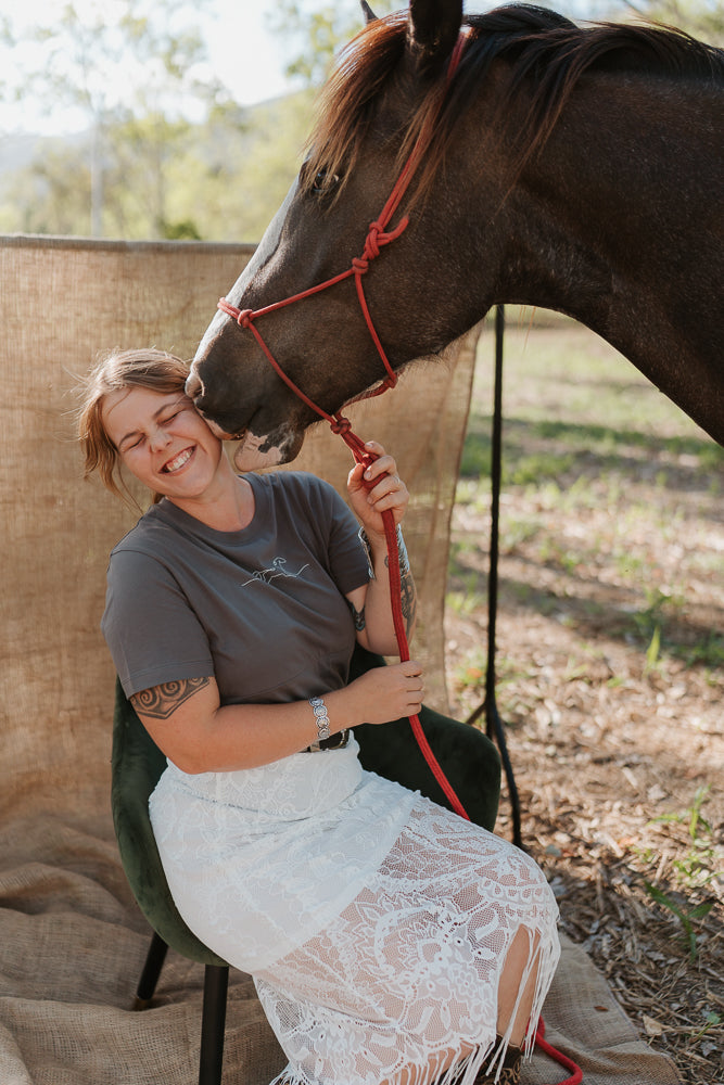 Woman sitting on a chair next to a horse, both interacting with each other outdoors.