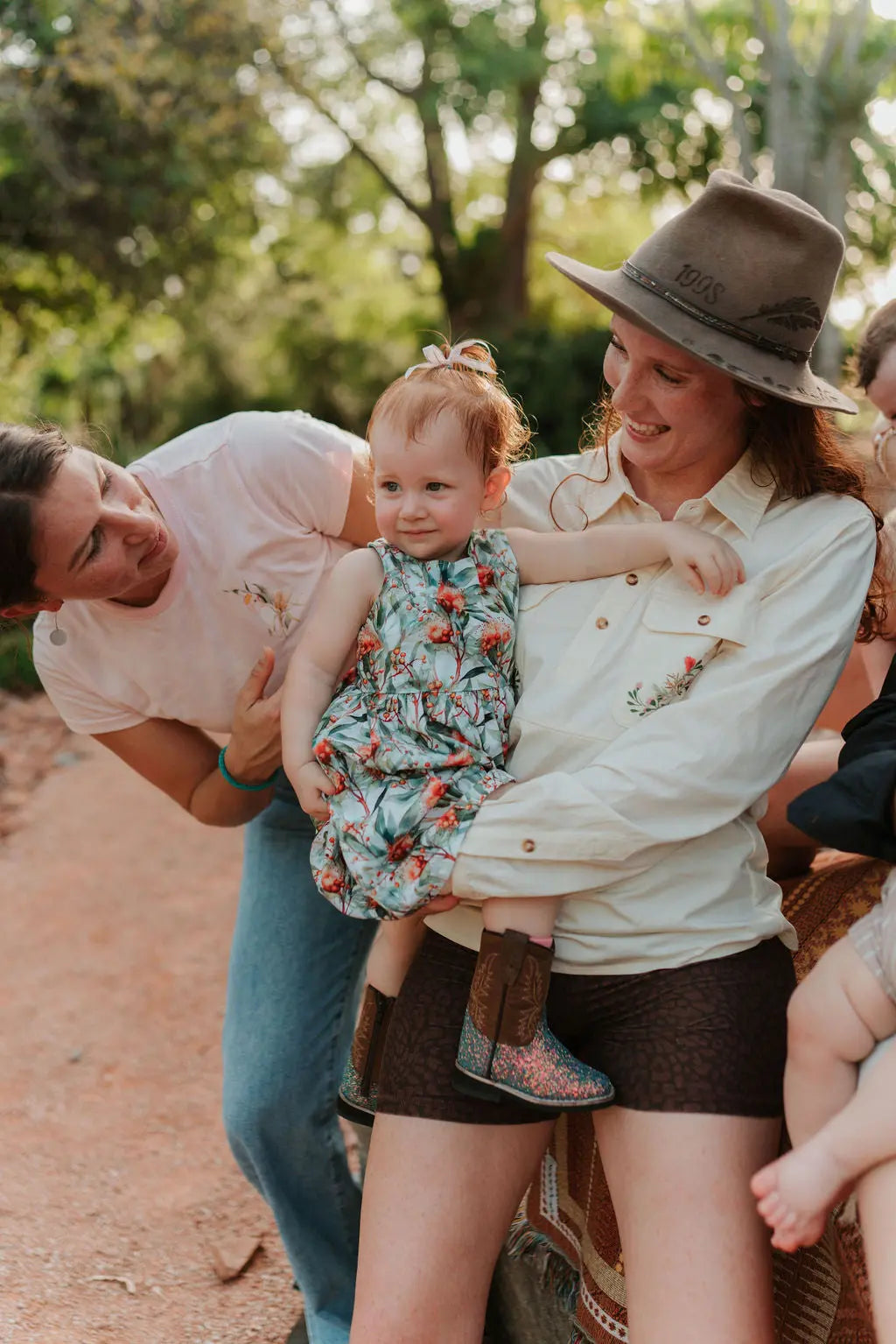 Woman holding a baby in a breastfeeding shirt with another woman in a shirt, outdoors, smiling.