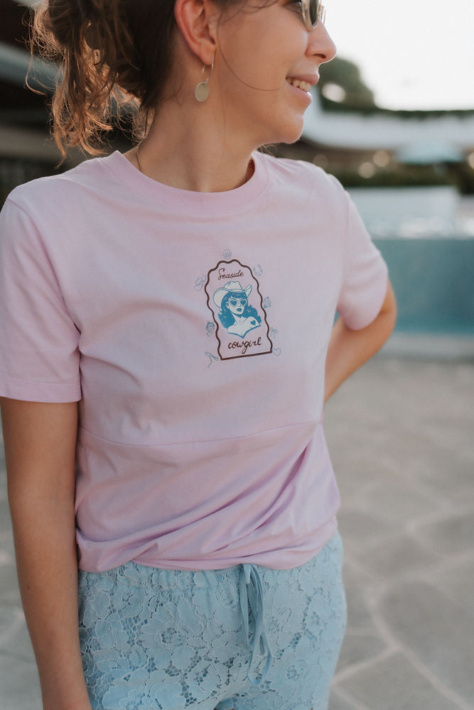 Person wearing a pink breastfeeding t-shirt with a graphic design, standing outdoors.