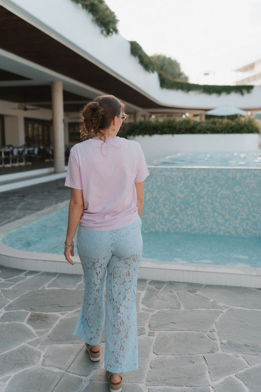 Woman standing by a poolside with a modern building in the background wearing postpartum lace long pants.