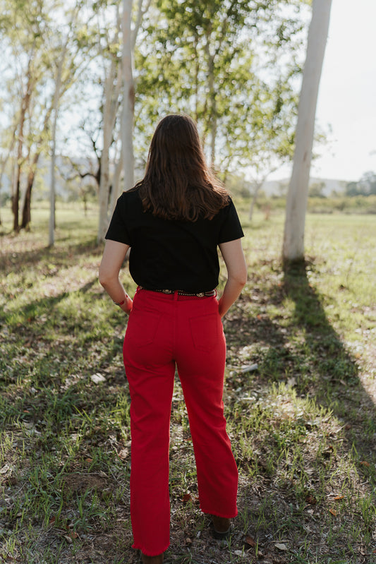 Person wearing a black shirt and red pants standing in a grassy field with trees.