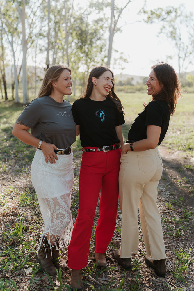 Three women standing outdoors in a natural setting, smiling and posing for the camera.