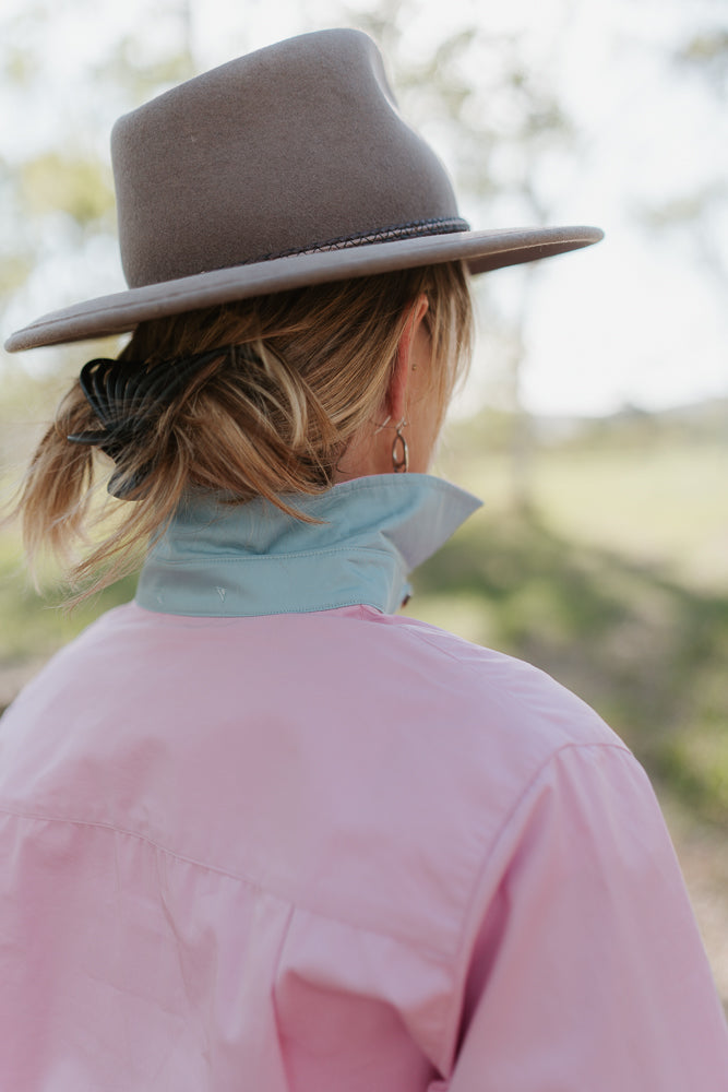 Person wearing a brown hat and pink shirt with a blurred natural background