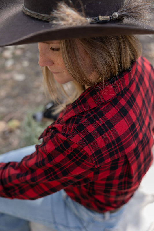 Person wearing a red and black plaid shirt with a cowboy hat outdoors.
