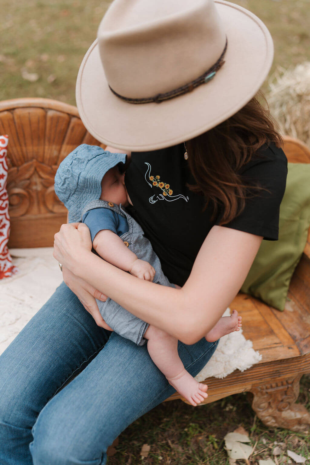 Person wearing a hat and black shirt holding a baby on a wooden bench outdoors.