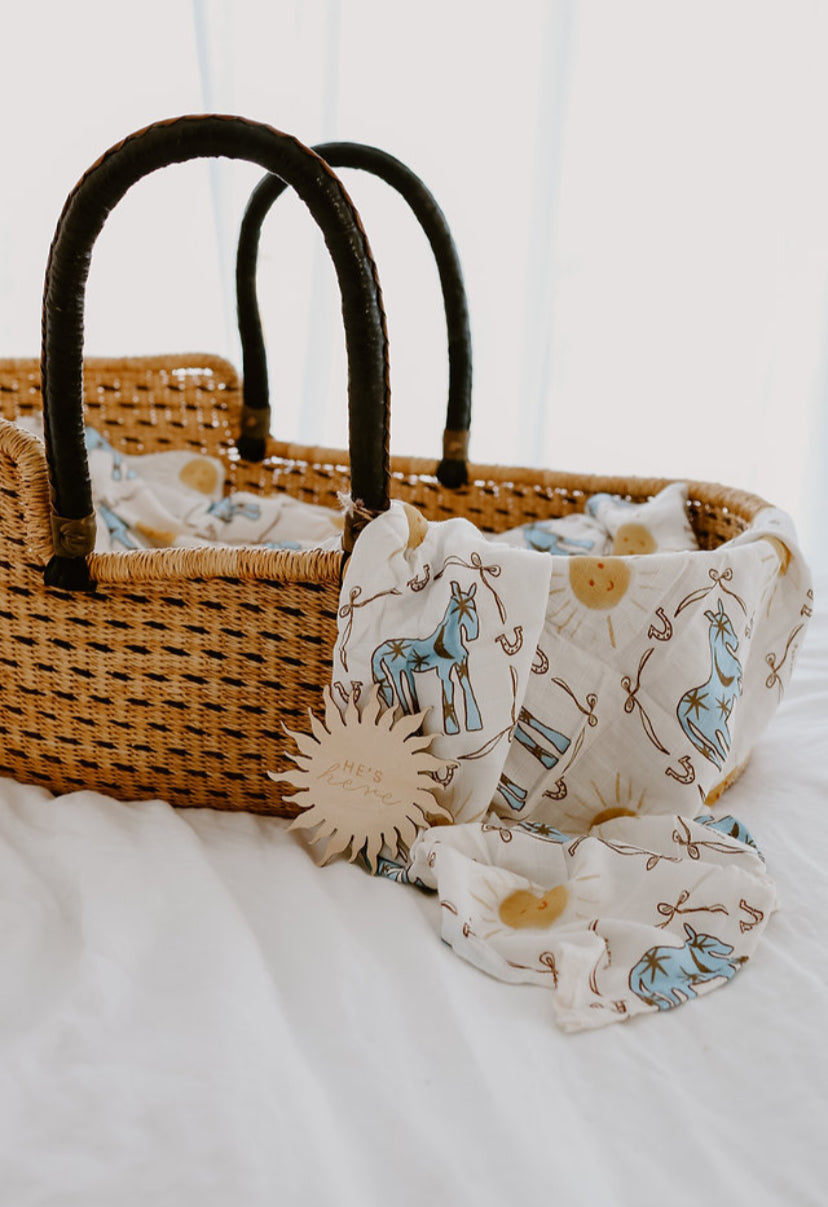 Wicker basket with baby items including a blanket with animal patterns on a white background