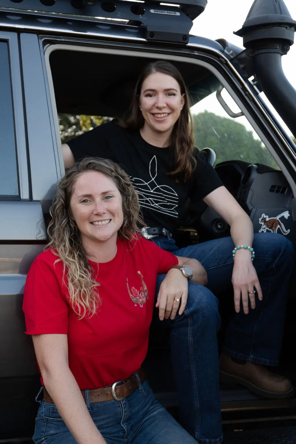 Two mums sitting in toyota ute smiling wearing breastfeeding shirts