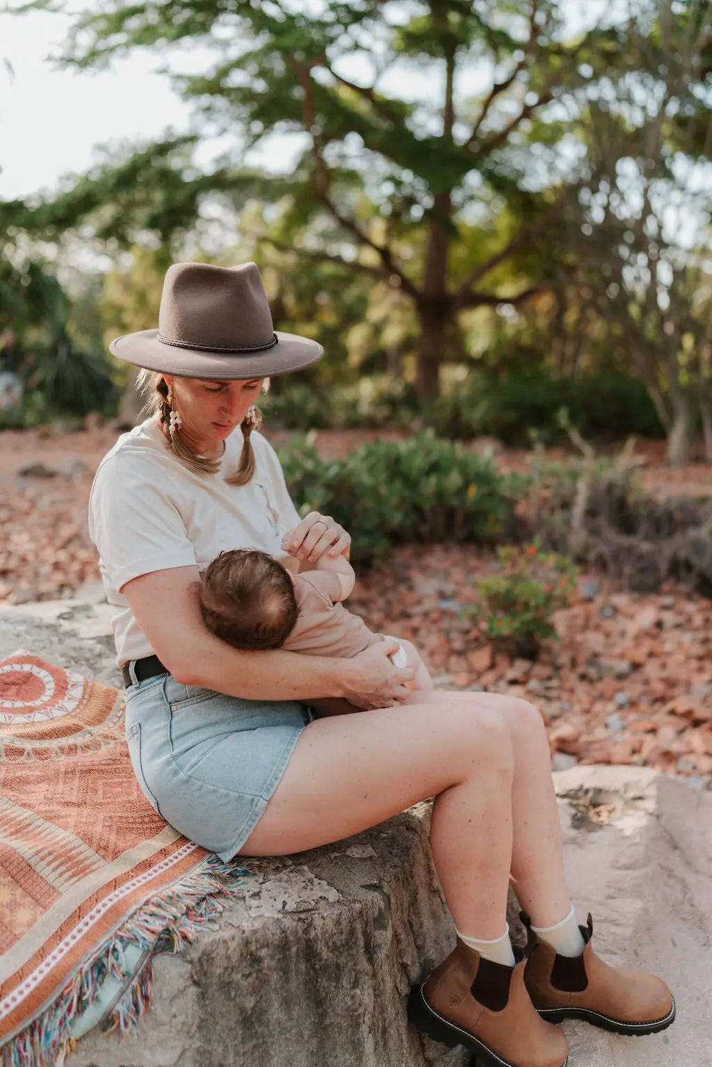 Woman sitting outdoors, breastfeeding a baby, wearing an Akubra hat and breastfeeding clothing.