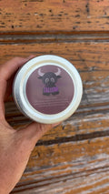 Hand holding a jar of tallow baby rash balm with a label on a wooden surface