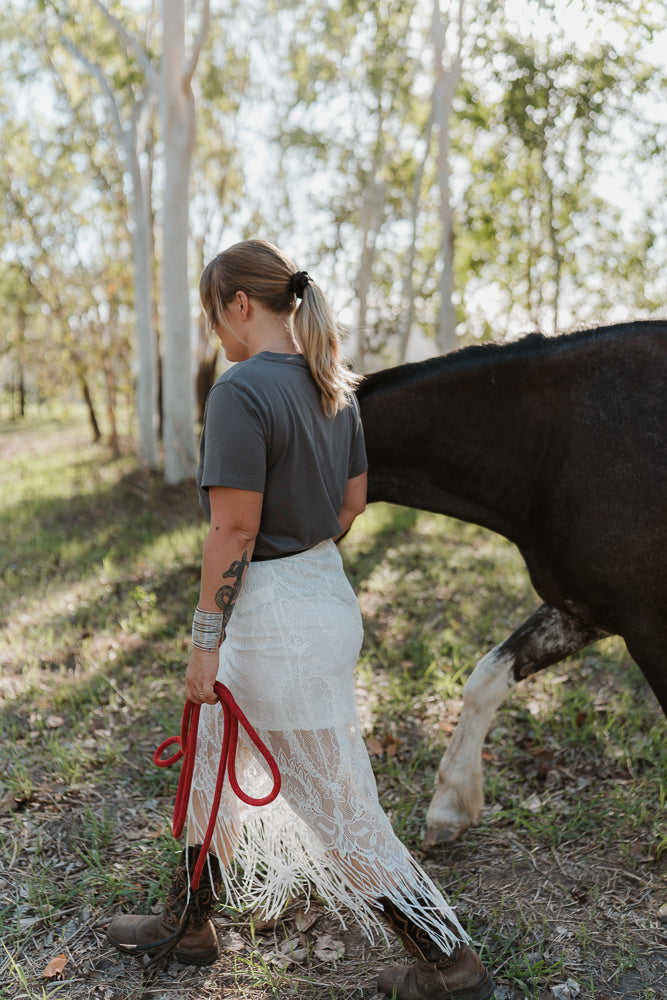 Woman standing next to a horse in a natural setting with trees in the background.