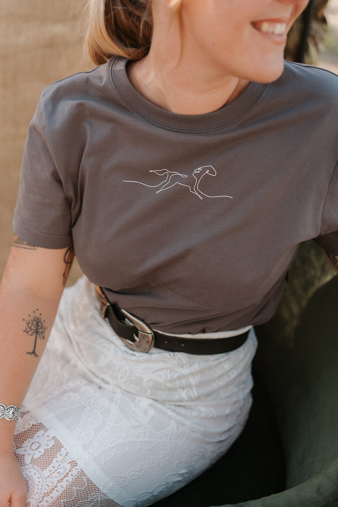 Person wearing a gray t-shirt with a white horse design, sitting outdoors.