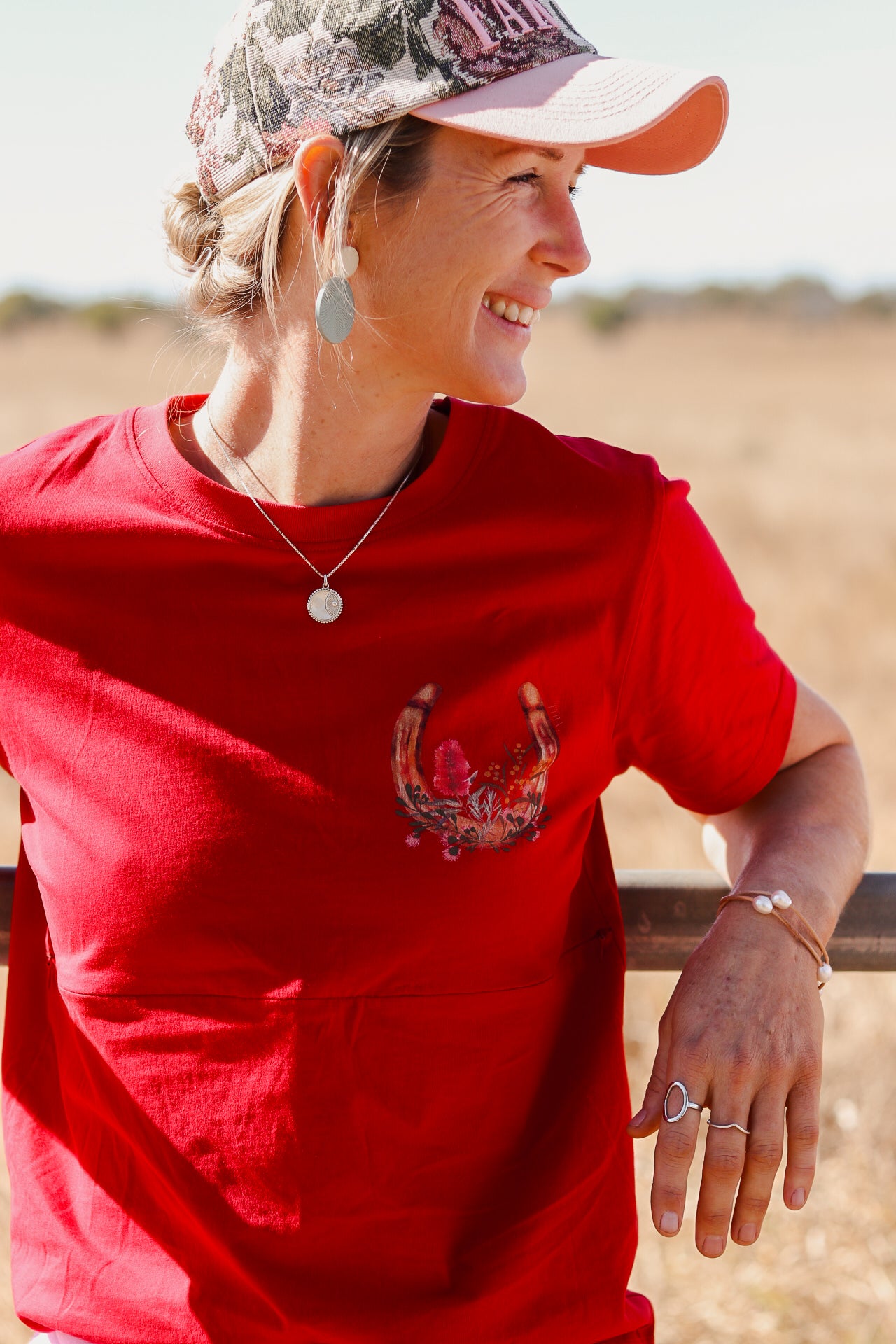mum wearing a red breastfeeding shirt featuring a horseshoe and bottlebrush print on the front