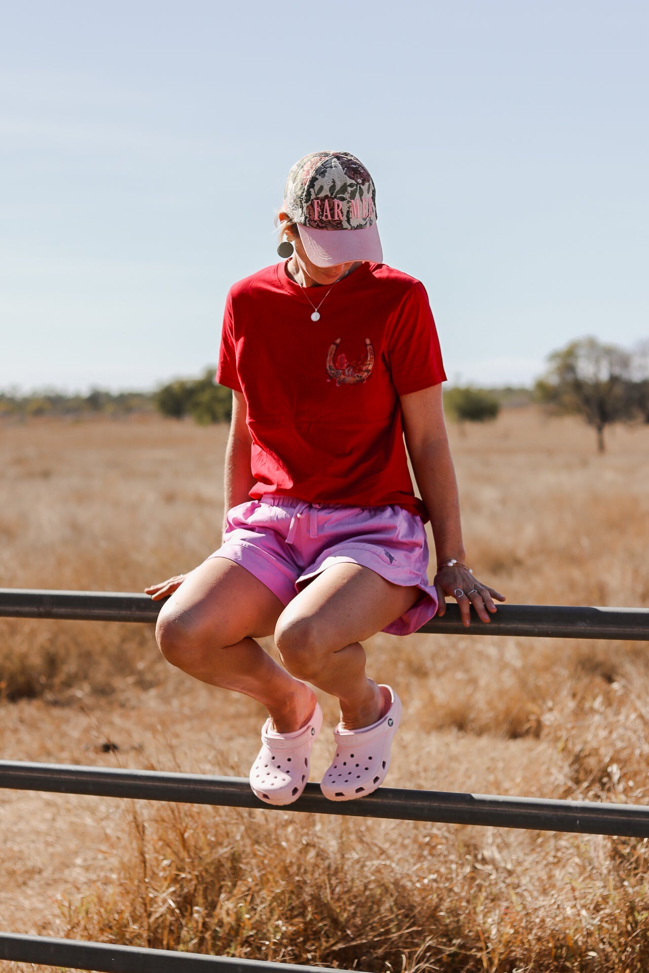 Person sitting on cattle rail fence wearing a red breastfeeding shirt featuring a horizontal breastfeeding zip.