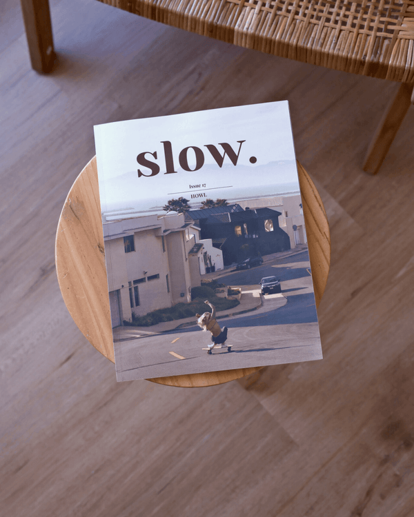 Magazine titled 'slow.' on a wooden stool with a wicker chair in the background