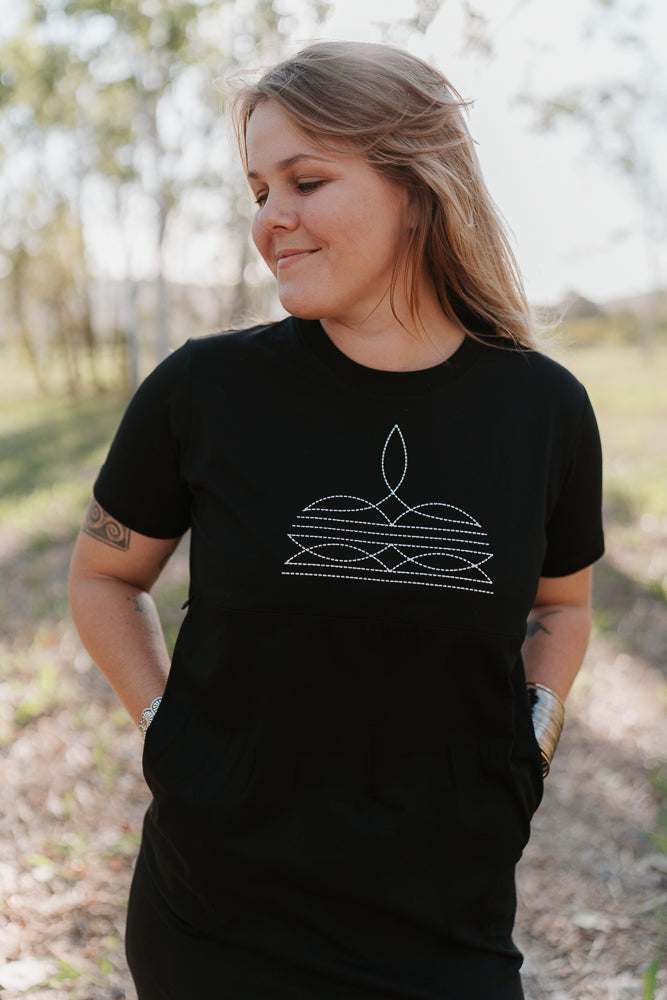 Woman wearing a black t-shirt dress with a white boot stitch design outdoors.