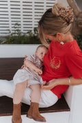 Woman in a red shirt breastfeeding a baby on a white bench outdoors.