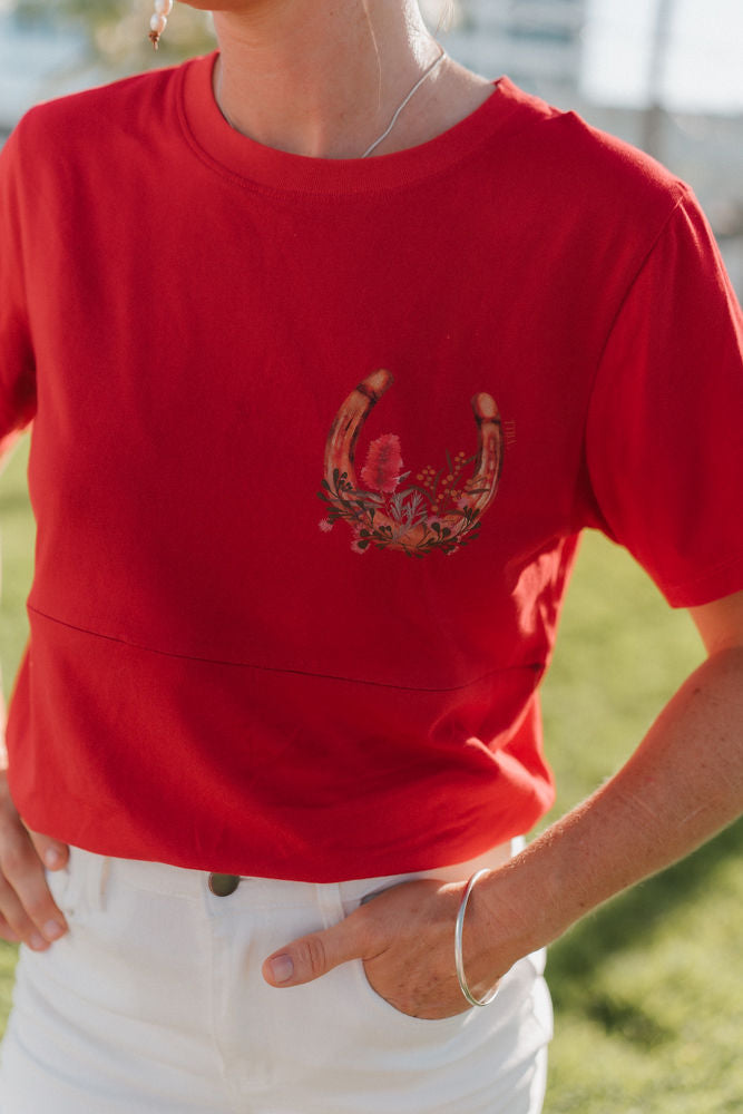 Person wearing a red nursing shirt with a floral native design outdoors.