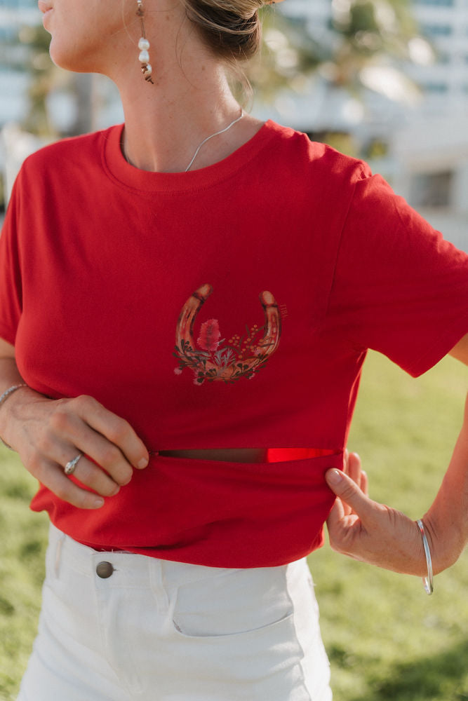 Person wearing a red nursing t-shirt with a native Australian flower design, standing outdoors. Showing a two way zip function. 