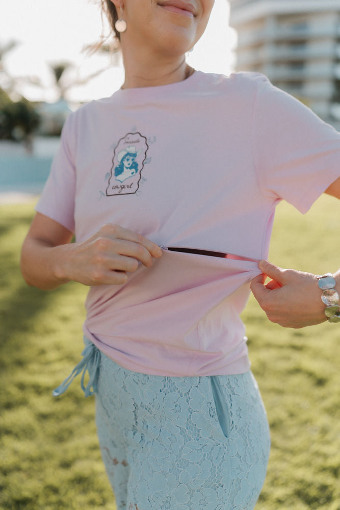 Person wearing a pink t-shirt with a graphic design, standing outdoors.showing function of two way breastfeeding zip. 