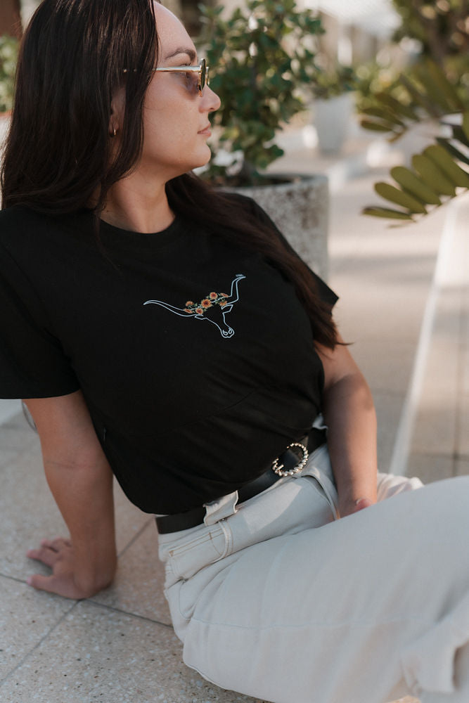 Woman wearing a black breastfeeding t-shirt with a graphic design, sitting outdoors.