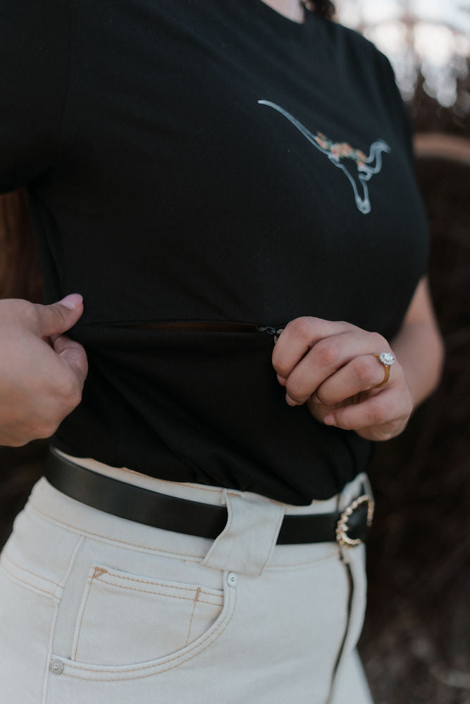 Person wearing a black nursing t-shirt with a logo and light-colored pants, showing the two way breastfeeding zip function their shirt.