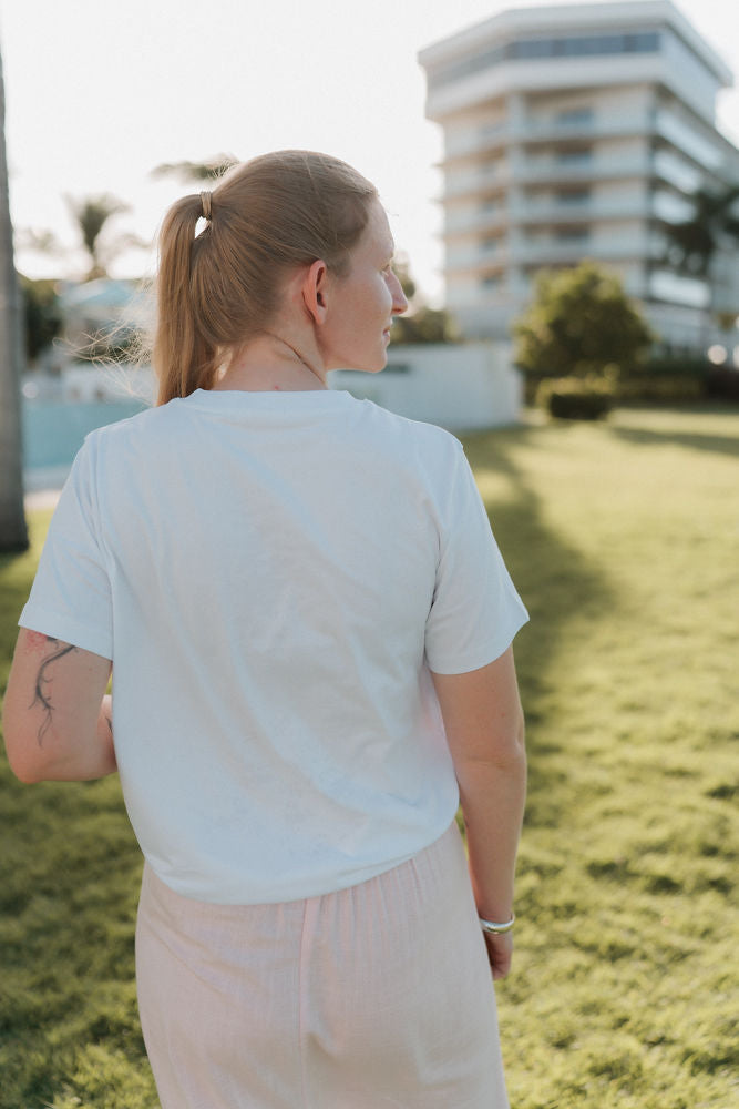Person wearing a white nursing t-shirt and light-colored pink skirt standing on grass with a building in the background
