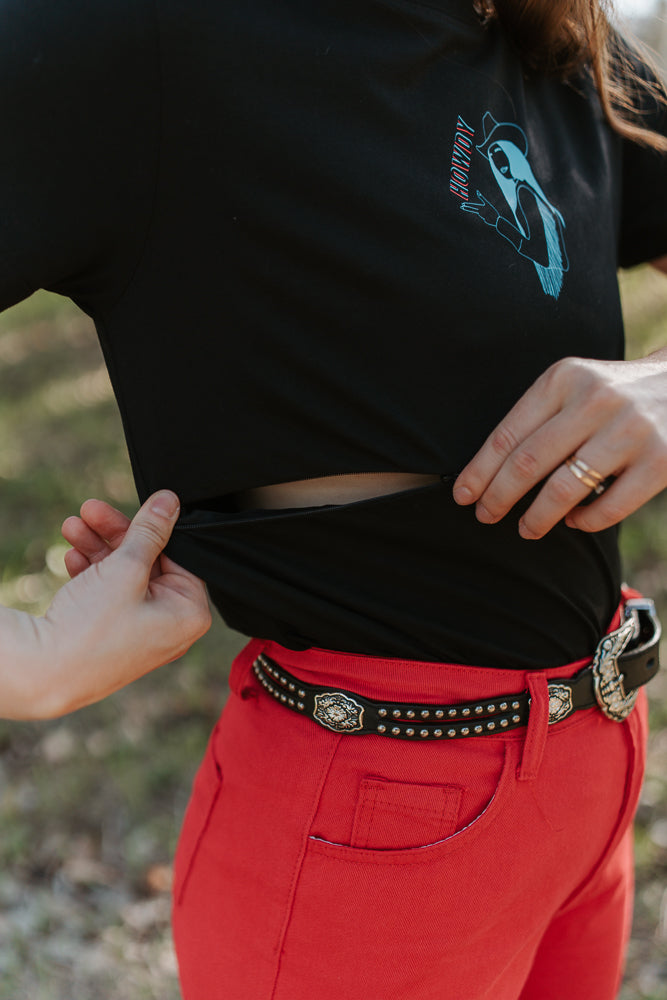 Person wearing a black shirt showing breastfeeding zip function with a graphic design and red pants outdoors.
