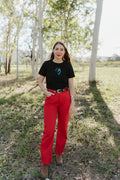 Woman wearing a black breastfeeding t-shirt and red pants standing in a bush area.