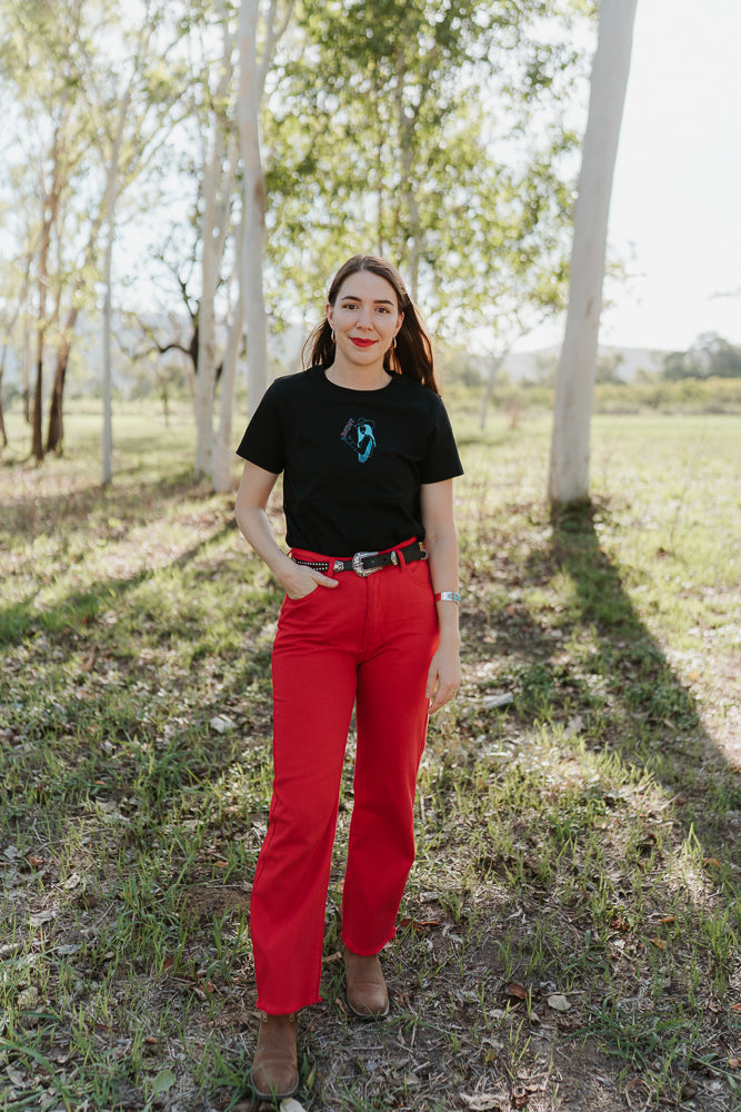 Woman wearing a black breastfeeding t-shirt and red pants standing in a bush area.