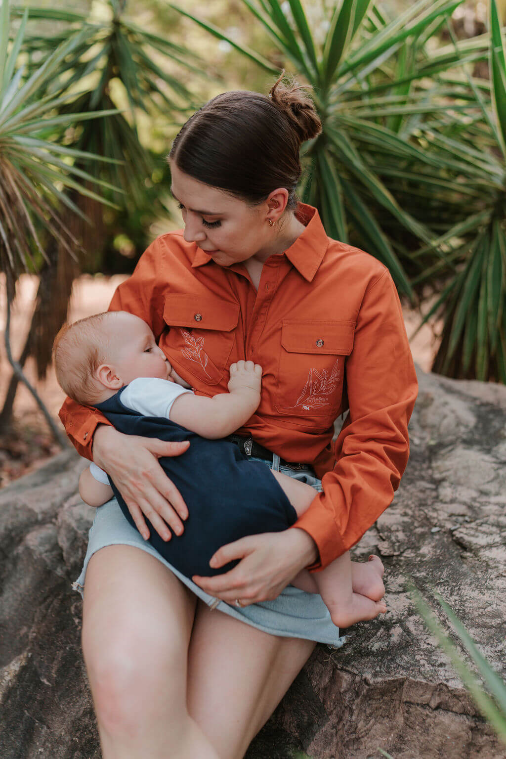 Mum sitting on rock outdoors while nursing baby 