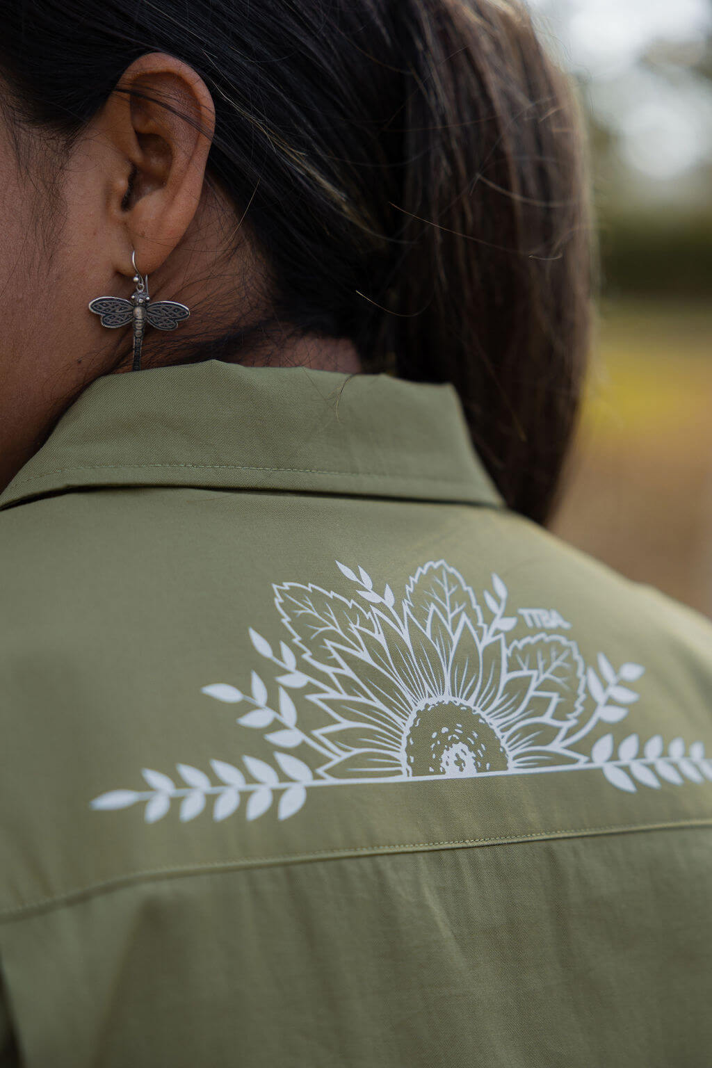 Green shirt with white floral design on the back, worn by a person outdoors.
