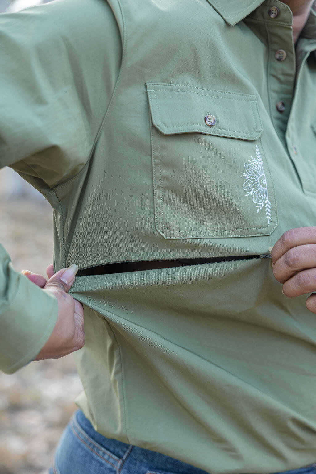 Person wearing a green shirt with a floral design on the chest pocket, standing outdoors.