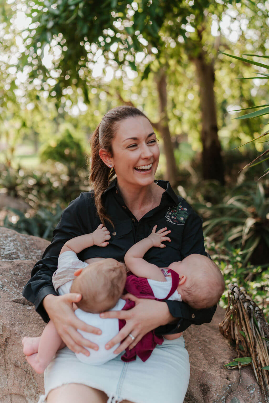 Mum sitting outdoors breastfeeding twins 