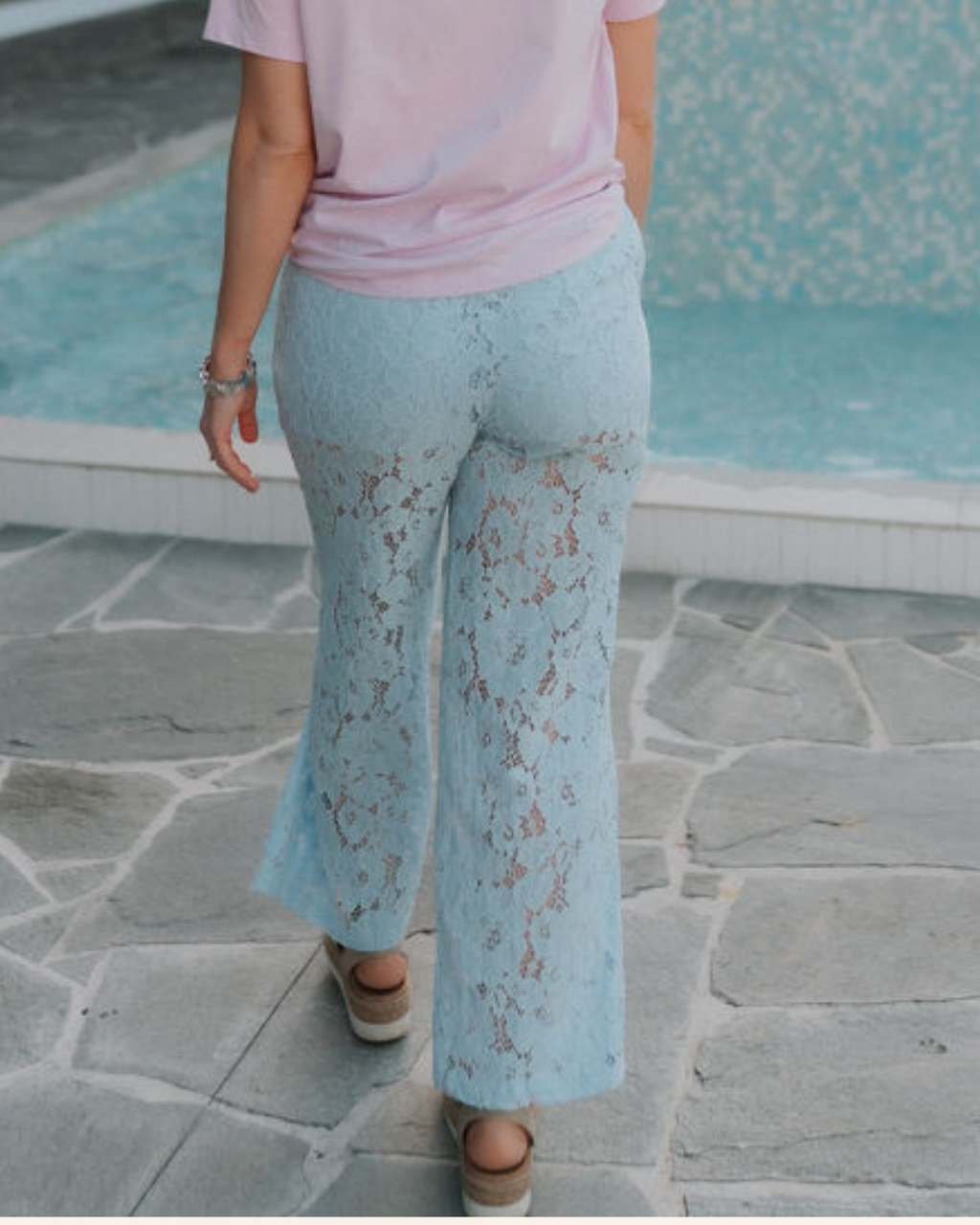 Person wearing light blue lace postpartum pants and a pink top by a pool