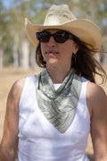 Woman wearing a cowboy hat and sunglasses with a patterned scarf, outdoors.